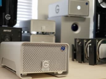 External Drive Recovery Close-up of multiple external hard drives on a desk. Foreground shows a silver GRIAD external drive, other hard drives blurred in the background.